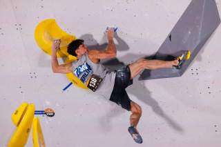 Mann mit Startnummer klettert an einer künstlichen Boulderwand