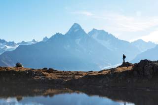 Ein Bild wie ein Scherenschnitt: ein Wanderer steht an einem See und blickt auf das alpin-gezackte Mont-Blanc-Massiv.