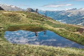 Zwei Mountainbiker fahren entlang eines Bergsees.