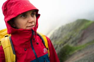 Eine junge Bergsteigerin in einer wasserdichten Makalu Gore-Tex Jacke Mountain Equipment, von deren Kapuze Regentropfen abperlen.