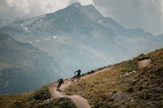 Zwei Mountainbiker auf einem Flowtrail vor Bergkulisse.