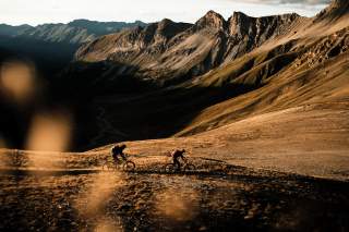 Zwei Mountainbiker fahren alpinen Rasen im gedämpften Herbstlicht.