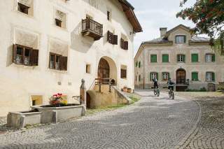 Zwei Mountainbiker fahren durch eine Dorfgasse mit bemalten Hausfassaden