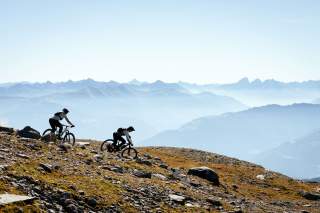Zwei Mountainbiker im alpinen Gelände vor Bergkulisse.