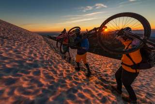 Mountainbiker tragen Fahrräder über Schneefeld am Berg