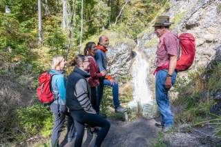 Gruppe von Menschen unterwegs am Berg, im Hintergrund ein kleiner Wasserfall