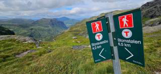 Große Wegweiser in grüner Fjelllandschaft, 4 Kilometer sind es zum Etappenziel Storavassbu.