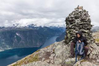 Ein junger Wanderer vor einer Steinpyramide über einem tief eingeschnittenen Fjord.