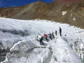 Gruppe von Menschen übt den Umgang mit Pickel und Steigeisen am Gletscher