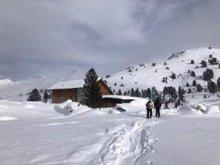 Zwei Menschen laufen durch tiefen Schnee auf Berghütte zu