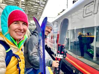 Zwei Menschen stehen mit Ski an Bahngleis