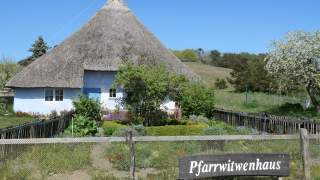 Hellblaues Häuschen mit Reetdach und Garten voller Blumen und Sträucher.