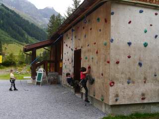 An einer etwa fünf Meter hohen Kletterwand an der Außenwand einer Berghütte erproben sich Kinder im Klettern.