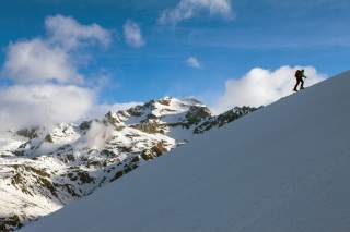 Mensch geht mit Ski steilen Schneehang hinauf