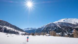 Mensch auf Schneeschuhen in sonnenbeschienener Winterlandschaft