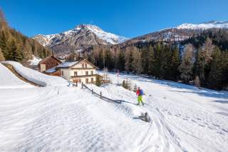Mensch läuft durch winterliche Landschaft auf Gasthaus zu