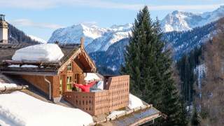 Mann steht auf Balkon in der Sonne und genießt verschneite Landschaft