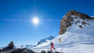 Mensch auf Tourenski in verschneiter Landschaft bei Sonnenschein