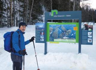Ein Skitourengeher steht vor einem Informationsschild der Kampagne 