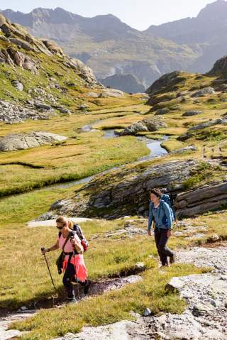 Zwei Menschen wandern durch Berglandschaft mit Bach