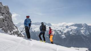 Drei Skibergsteiger blicken von der Montasio-Seite auf die Gipfel der Kanin-Gruppe.