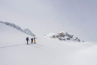 Drei Skitourengeher ziehen ihre Spur, im Hintergrund die Felsgipfel im Kanin-Gebiet.