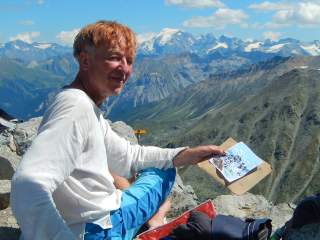 Hans-Christian Hauser blickt in die Kamera, in der Hand ein gemaltes Bild, im Hintergrund ein Alpenpanorama