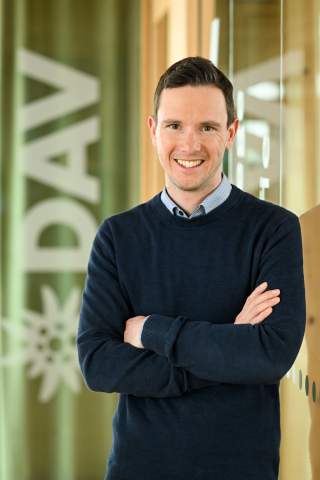Dominik Birnbacher steht vor einer Glaswand mit DAV Logo