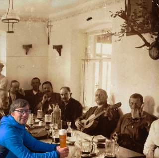 Fotomontage aus altem und neuem Bild; mehrere Männer sitzen am Tisch im Gastraum einer Hütte, einer spielt Gitarre.