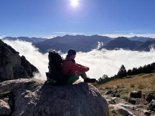 Mann sitzt auf Fels in den Bergen und genießt die Aussicht