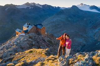 Zwei Wandernde vor Hütte im Hochgebirge