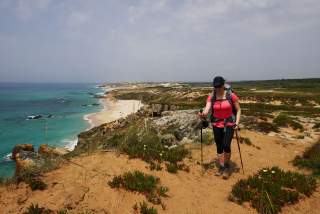 Wanderin mit Rucksack und Stöcken wandert über Sand an der portugiesischen Steilküste