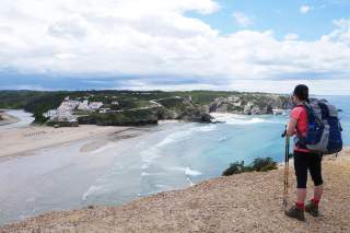 Wanderin blickt von der Steilküste hinunter auf eine Bucht mit Sandstrand.