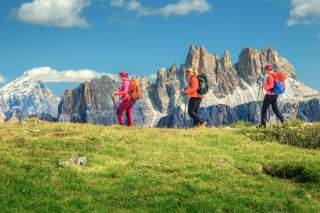 Drei Frauen mit Rucksack vor Dolomitenrucksäcke, sie laufen von rechts nach links durchs Bild.