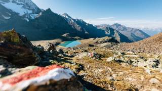 Kleiner türkiser Gebirgssee umgeben von zackigen Gipfeln und braunem Gestein.