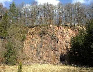 Das Foto zeigt eine Nahaufnahme einer der Felsen der Bruchhauser Steine. Zu sehen ist die stark verzackte Kante, im Hintergrund ist aufgrund der niedrigen Perspektive nur blauer Himmel zu sehen. Im Vordergrund des Fotos hängen einige grüne Laubbaumzweige ins Bild. Die Felswand selbst sehr uneben aber stabil. Die Bruchhauser Steine dienen als gutes Beispiel für die Felsformationen im Sauerland, sind jedoch aus naturschutzgründen für das Klettern gesperrt. Das Foto dient zur Repräsentation der Kletterregion.