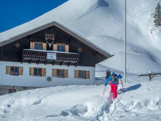 Mensch auf Schneeschuhen läuft auf verschneite Hütte zu