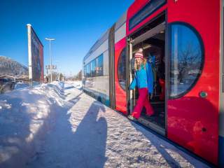 Schneeschuhgeherin steigt aus einem Zug aus in verschneiter Landschaft.