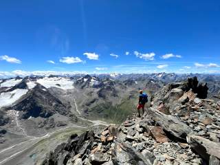 Mensch steht auf felsigem Gipfel und genießt den Ausblick übers Gipfelmeer