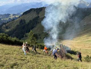 Mehrere Personen verbrennen Schnittgut von einer Schwendaktion am Berg.
