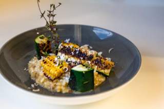 Steinpilzrisotto, angerichtet in einem tiefen Teller, mit Zucchini und Maiskolben arrangiert.