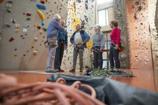 Gruppe älterer Menschen steht mit Ausrüstung in Kletterhalle