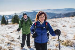 Ein älteres Paar mit Wanderstöcken bei sonnig-winterlichen Bedingungen am Berg.