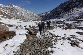 Fünf Bergsteiger steigen über schneebedecktes Geröll im Hochgebirge.