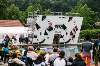 Publikum beobachtet einen Boulderwettkampf an einer künstlichen Kletterwand über einem Wasserbecken im Freien.