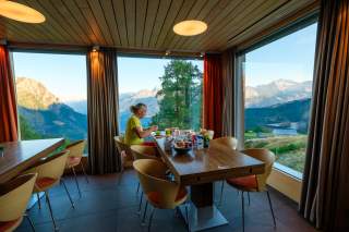 Person sitzt bei Frühstück in Berghotel mit Ausblick auf Bergkette