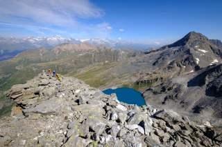 Gruppe steigt durch plattige Berglandschaft auf, unten sieht man einen blauen Bergsee