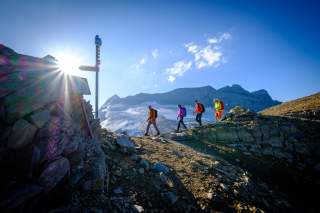 Vier Personen wandern durchs Gebirge, im Hintergrund Berge mit Gletschern