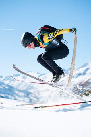 Franz Eder zieht beim Skimo-Training mit einem kräftigen Sprung nach oben die Felle von seinen Skiern ab, vor schöner Bergkulisse.