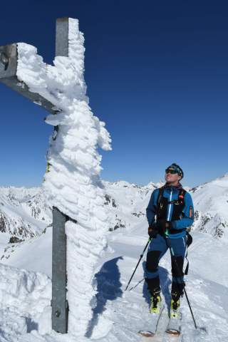 Gipfelkreuz mit Raureif bedeckt und Skitourengeher